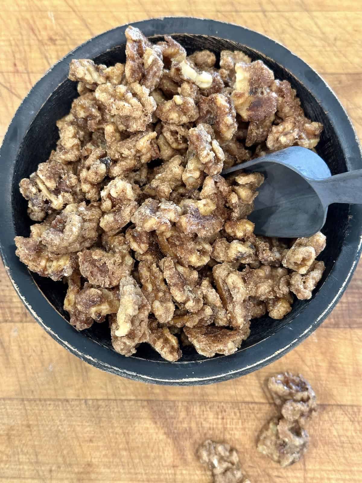 Spiced walnuts in a serving bowl with a small scoop on a cutting board.