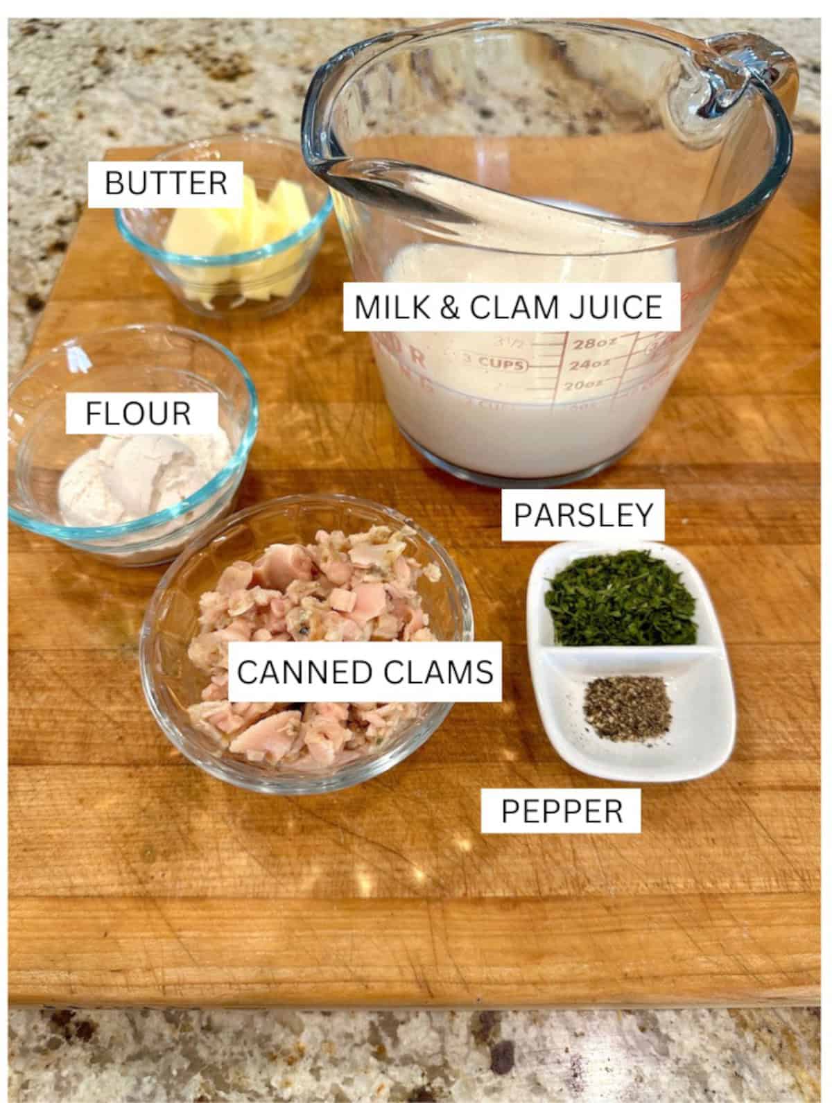 Ingredients for white clam sauce in small bowls with labels, on a cutting board.