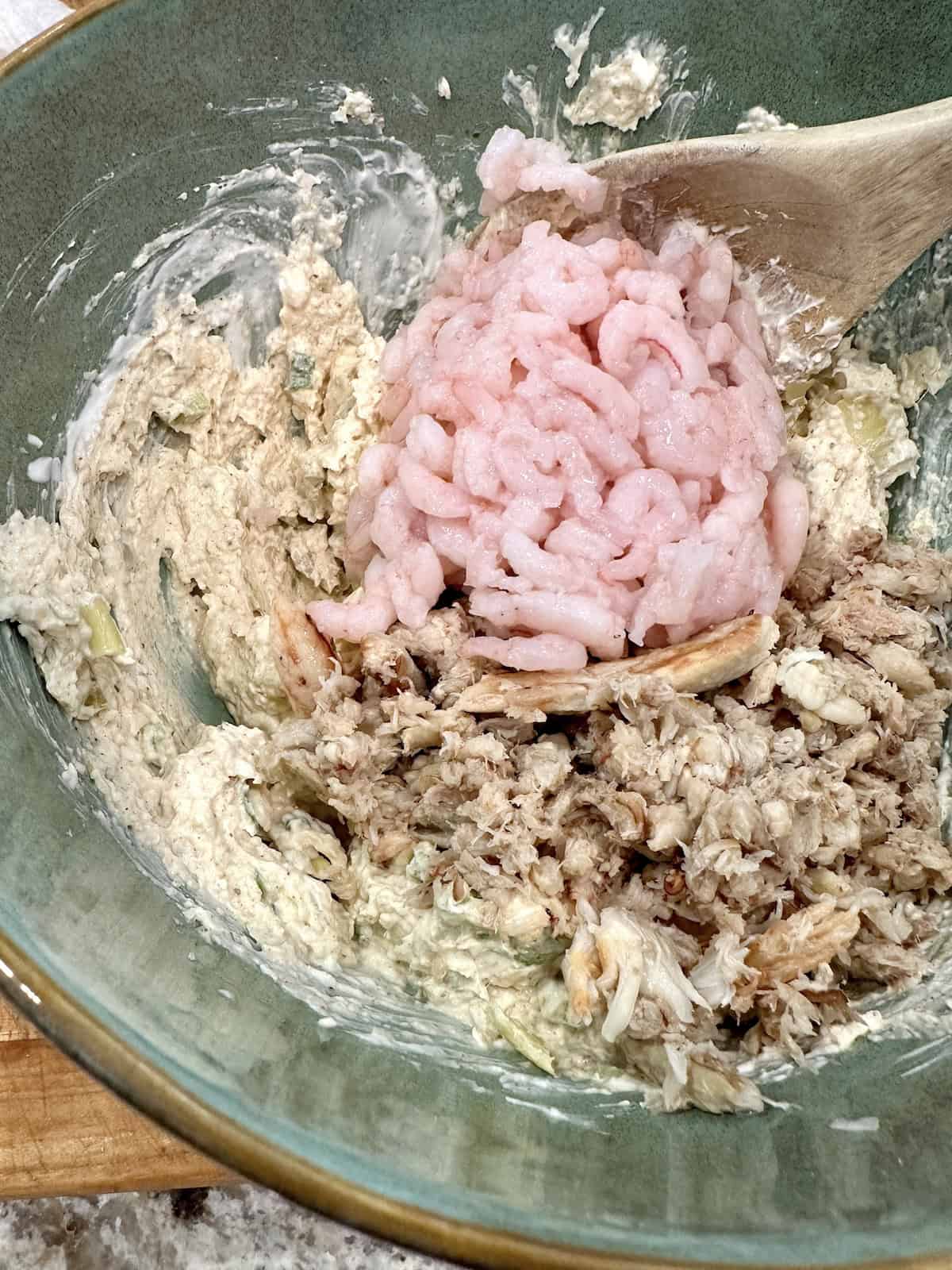 Shrimp and crab are added to a dip mixture in a bowl.