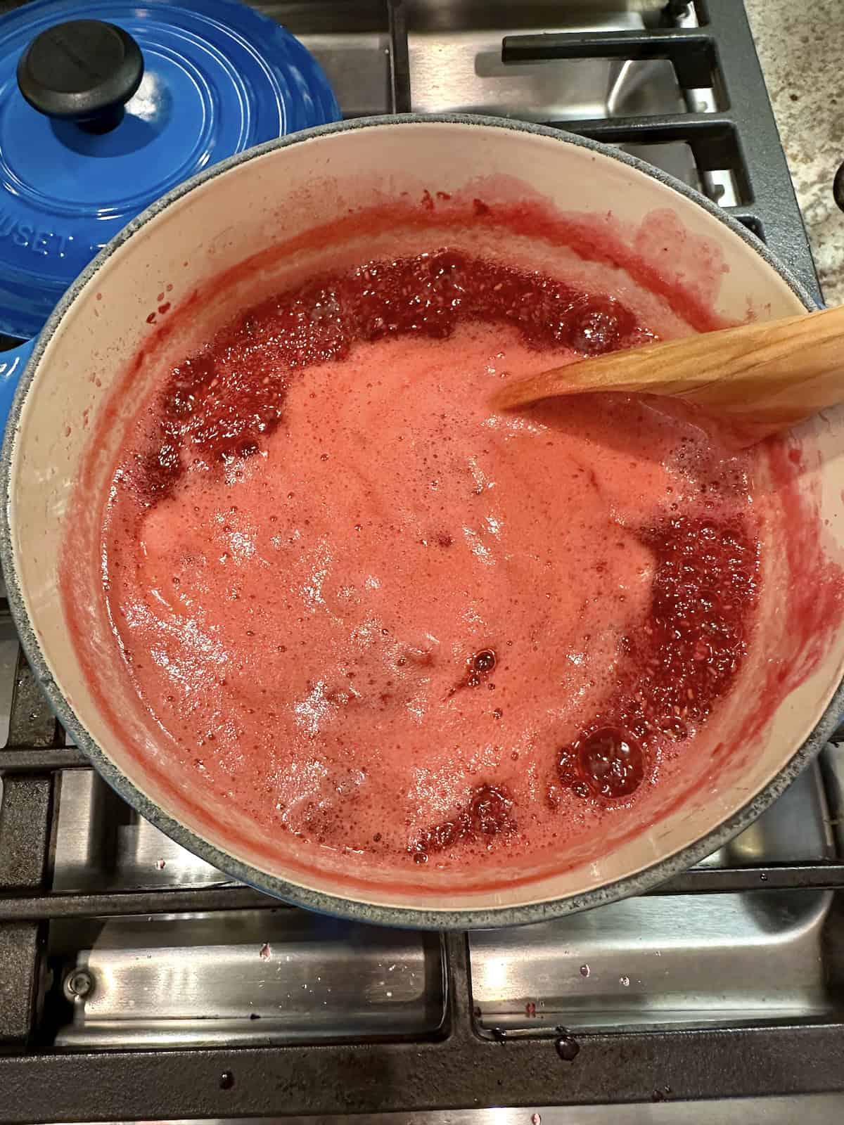 Raspberry jam simmering in a pan on the stove.