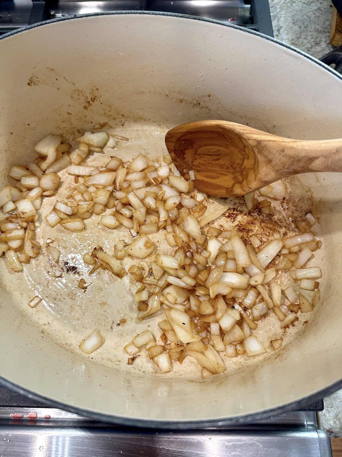 Diced onions in a pan with a wooden spoon.