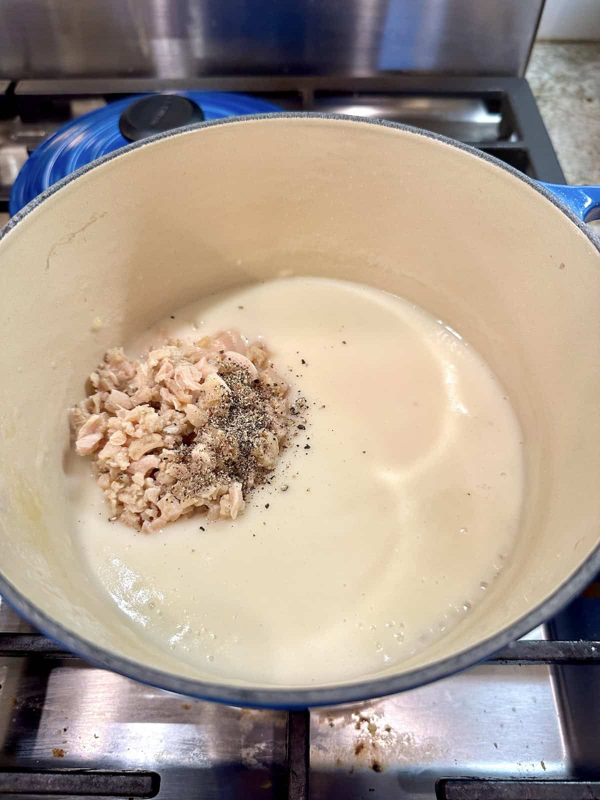White canned clam sauce in a pan on the stove with clams and pepper.