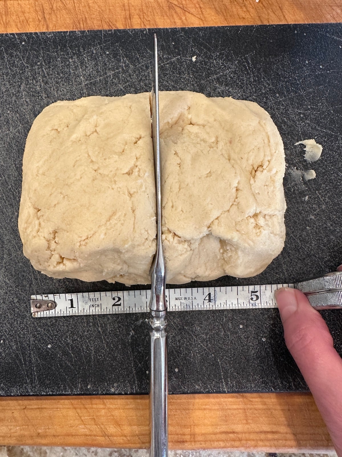 Unbaked holiday cookie dough on a cutting board with a knife and measuring stick.