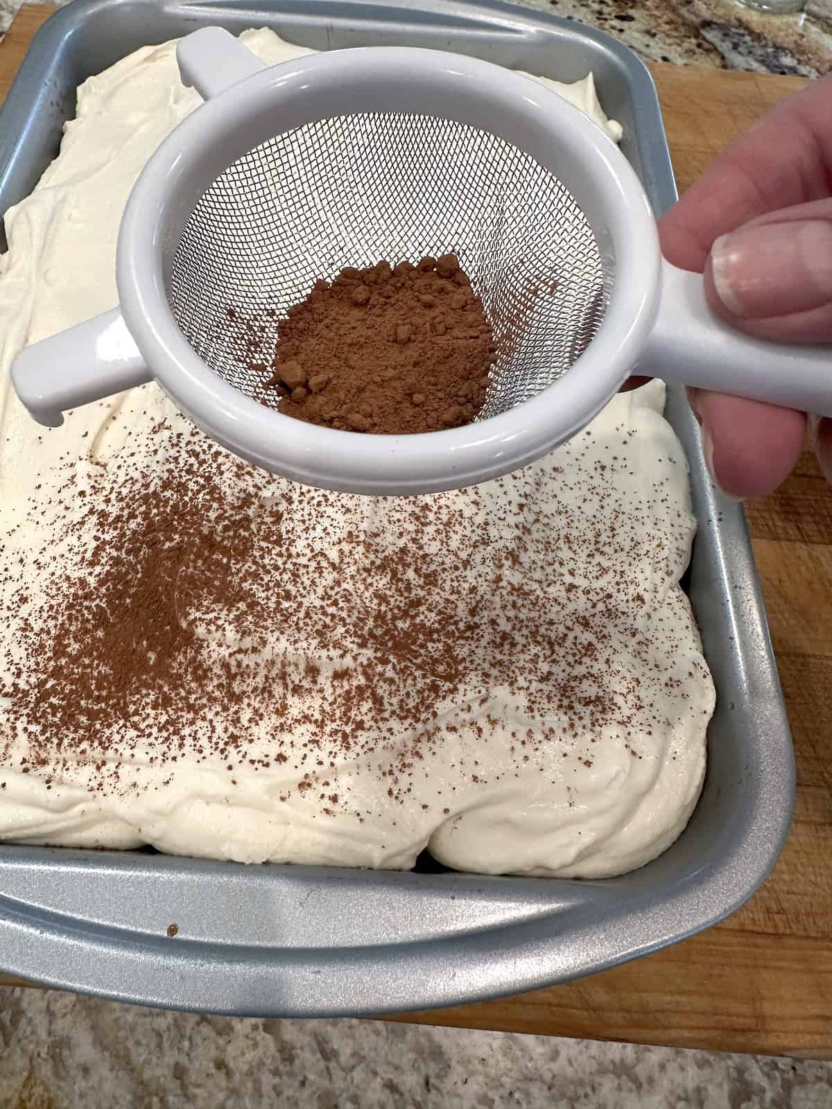 A strainer of cocoa powder over a tiramisu cake with mascarpone frosting.