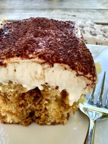 A serving of tiramisu cake on a plate with a fork.