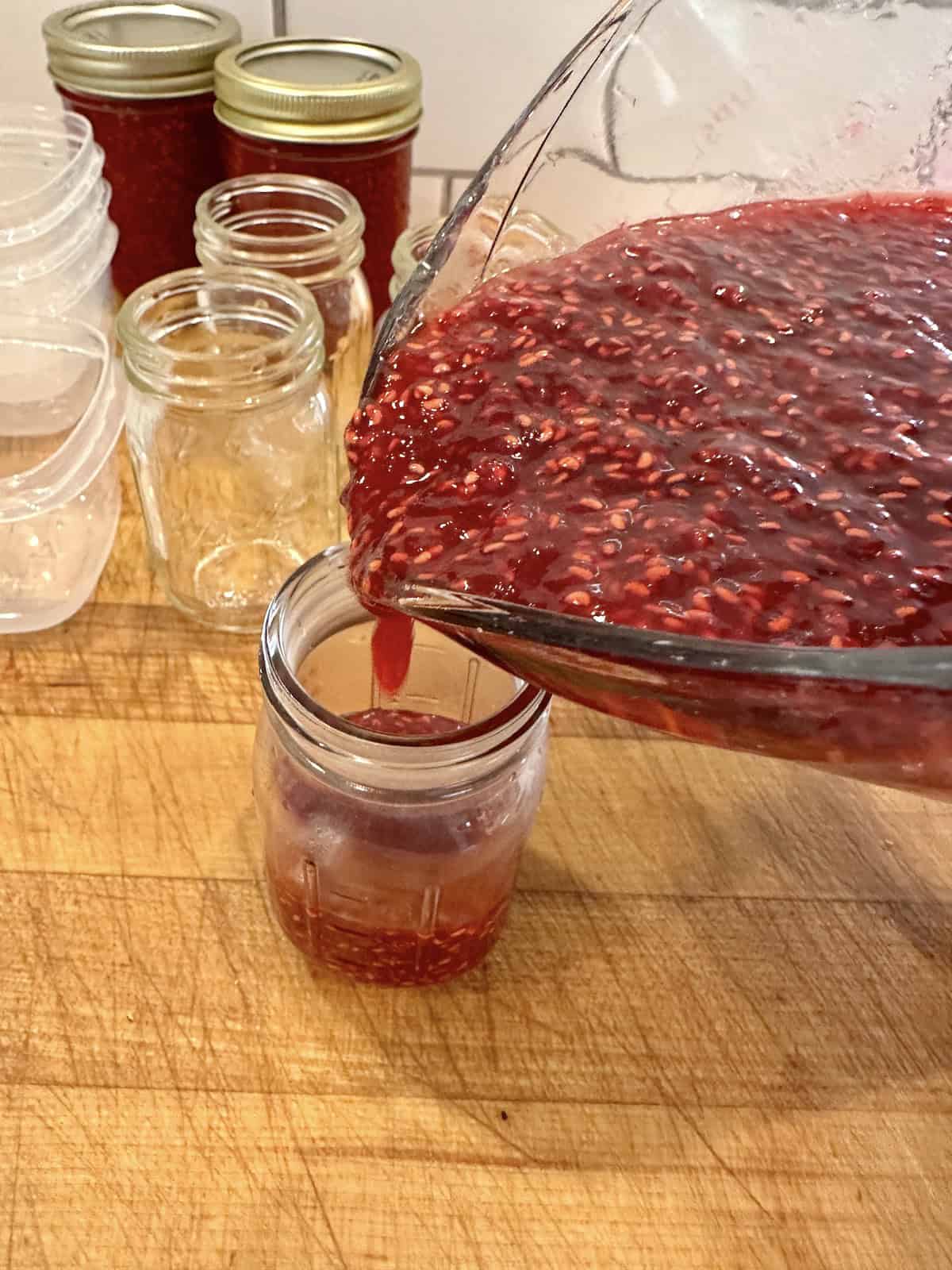 A small jar being filled with raspberry jam.