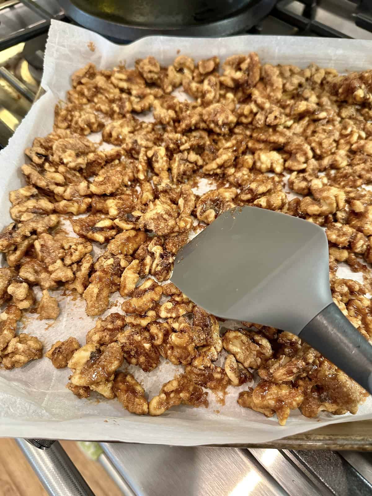 Oven-roasted spiced walnuts cooling on parchment paper with a spatula.
