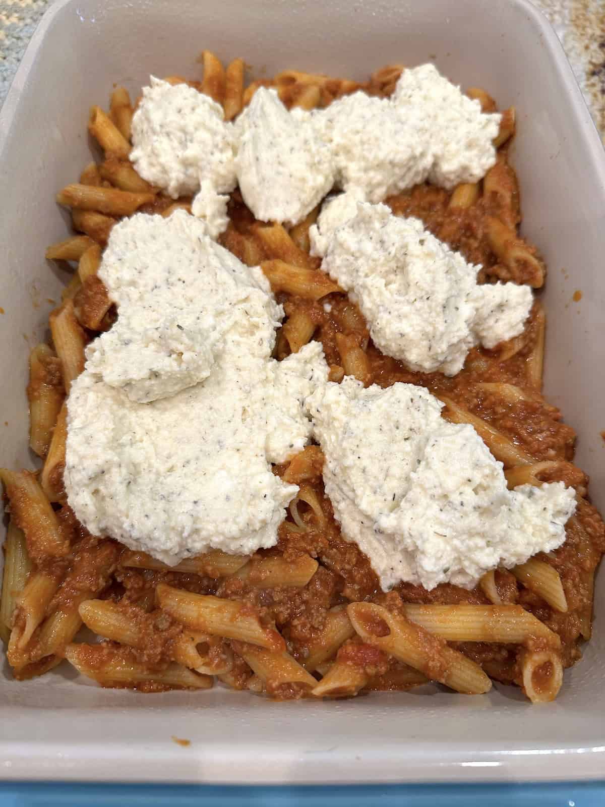 Unbaked lazy lasagna in a baking dish with ricotta cheese on top.