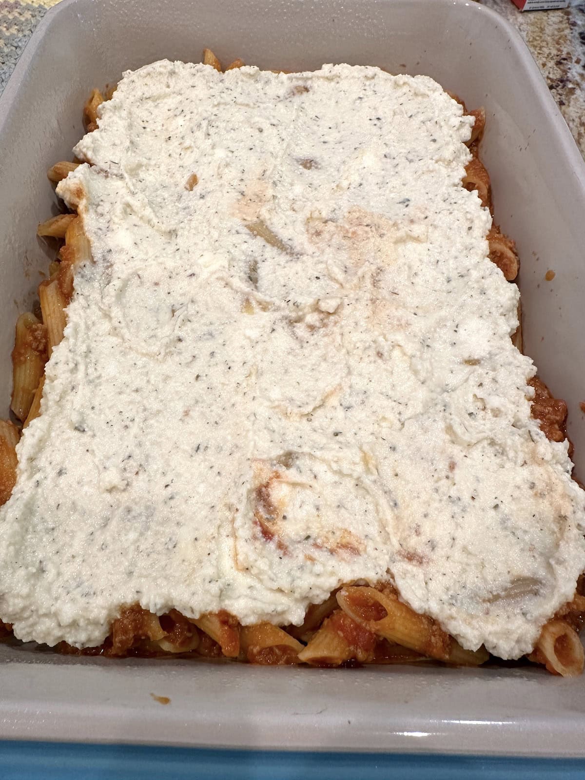 Ricotta cheese covered a layer of pasta, meat and cheese in a baking dish.