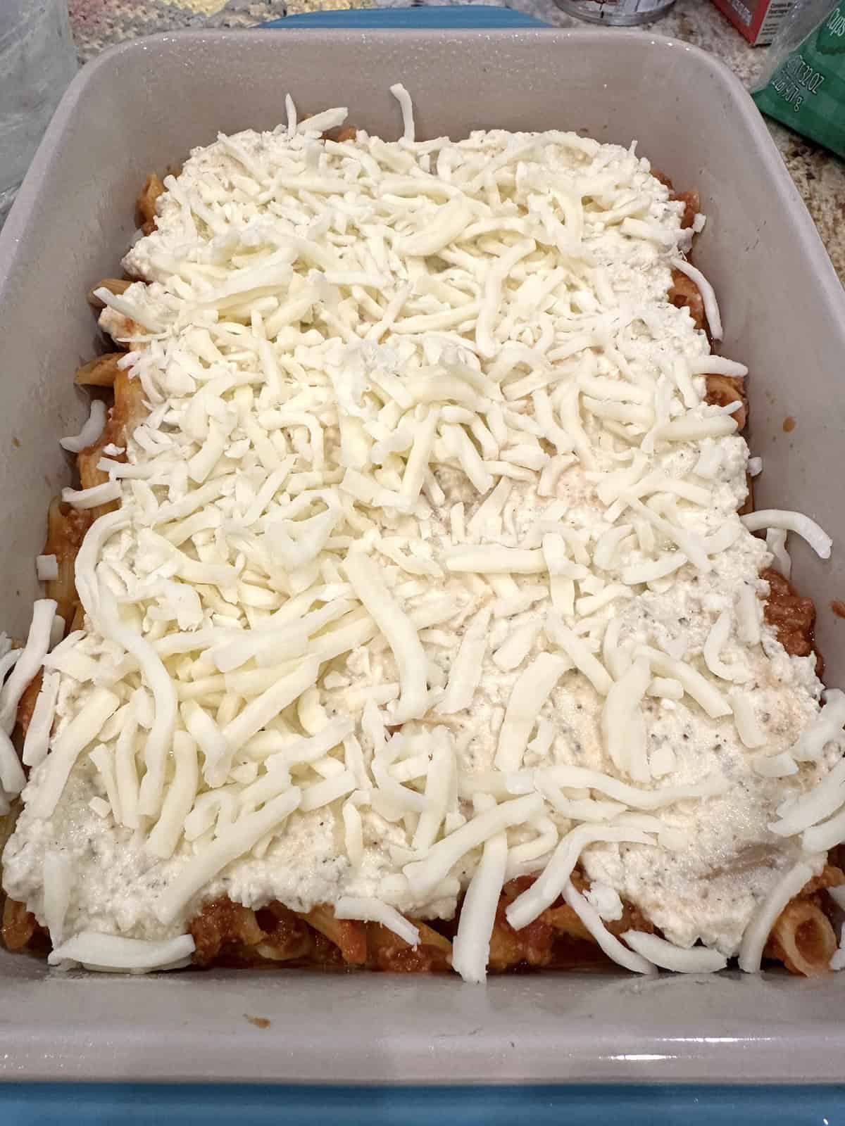 Mozarella cheese and ricotta on top of pasta noodles in a baking dish.