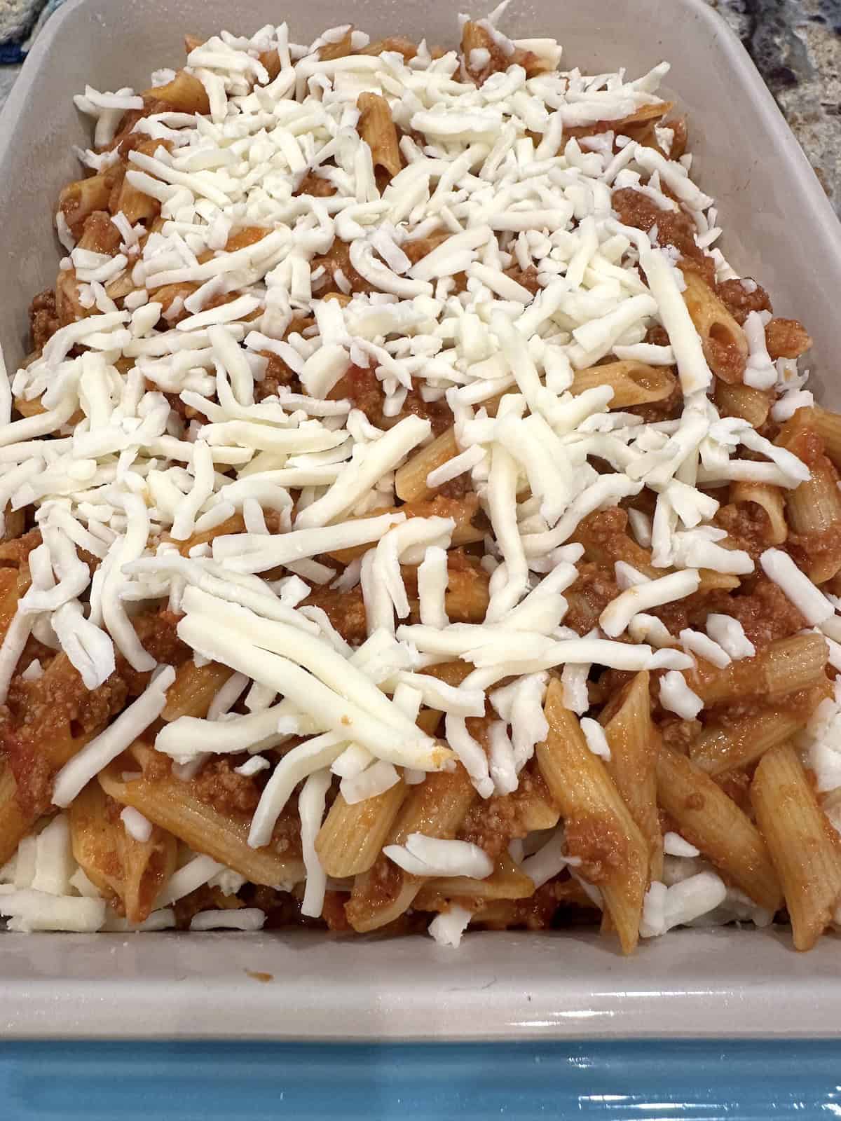 Unbaked pasta, sauce and meat in a baking dish with mozzarella cheese on top.