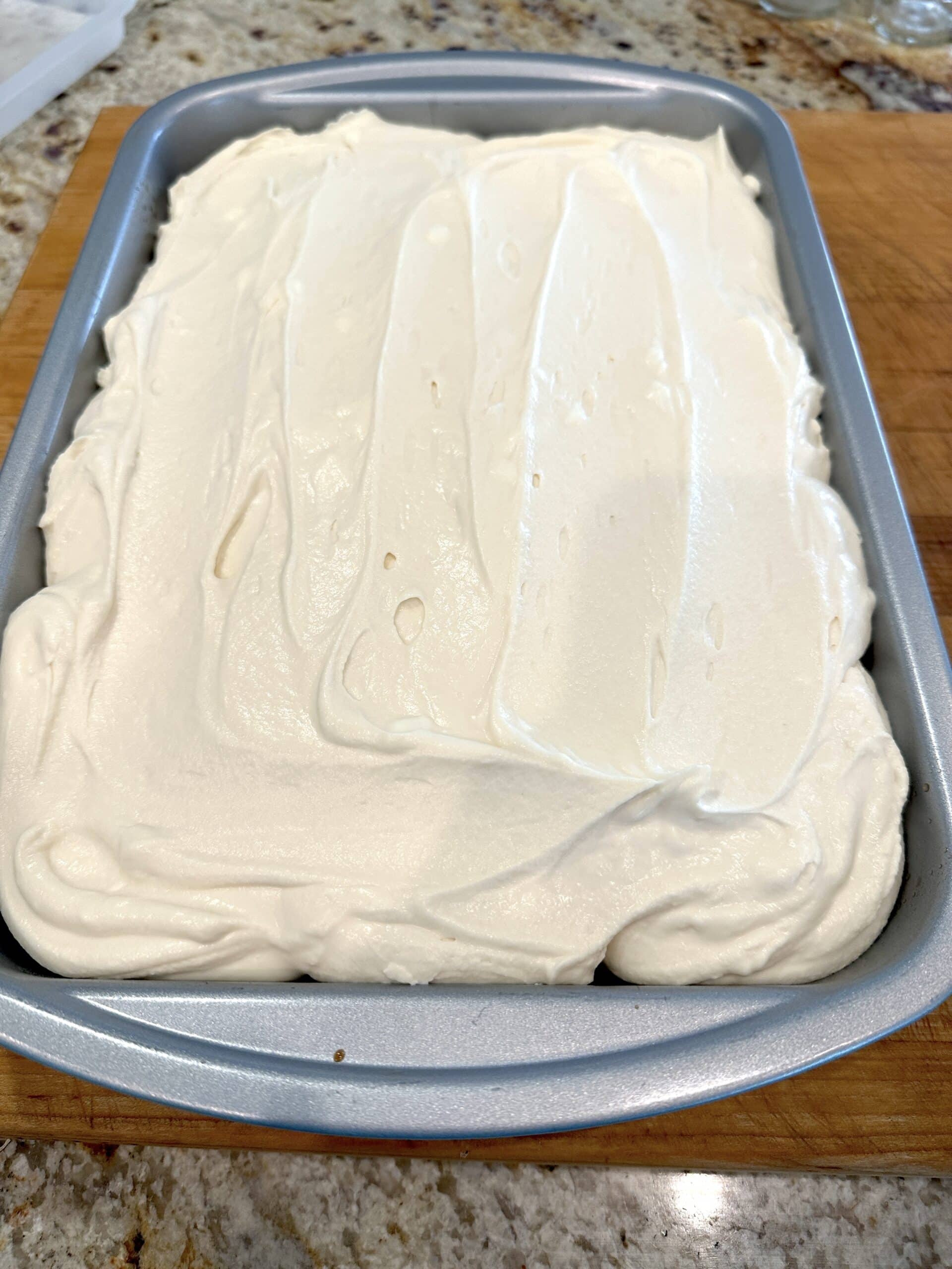 Mascarpone frosting on top of a cake in a baking dish.