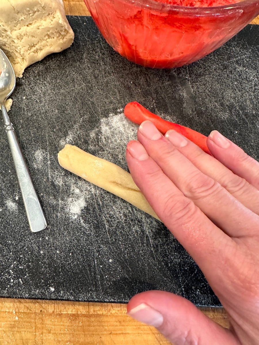 Rolling candy cane cookie dough on a cutting board.