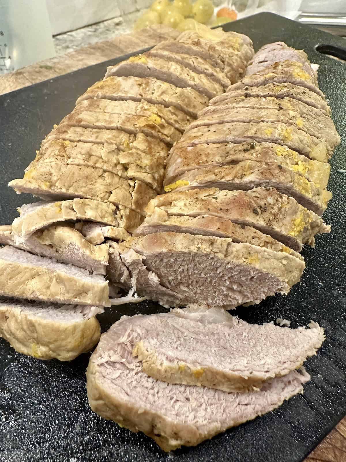 Sliced, cooked pork tenderloin on a cutting board.
