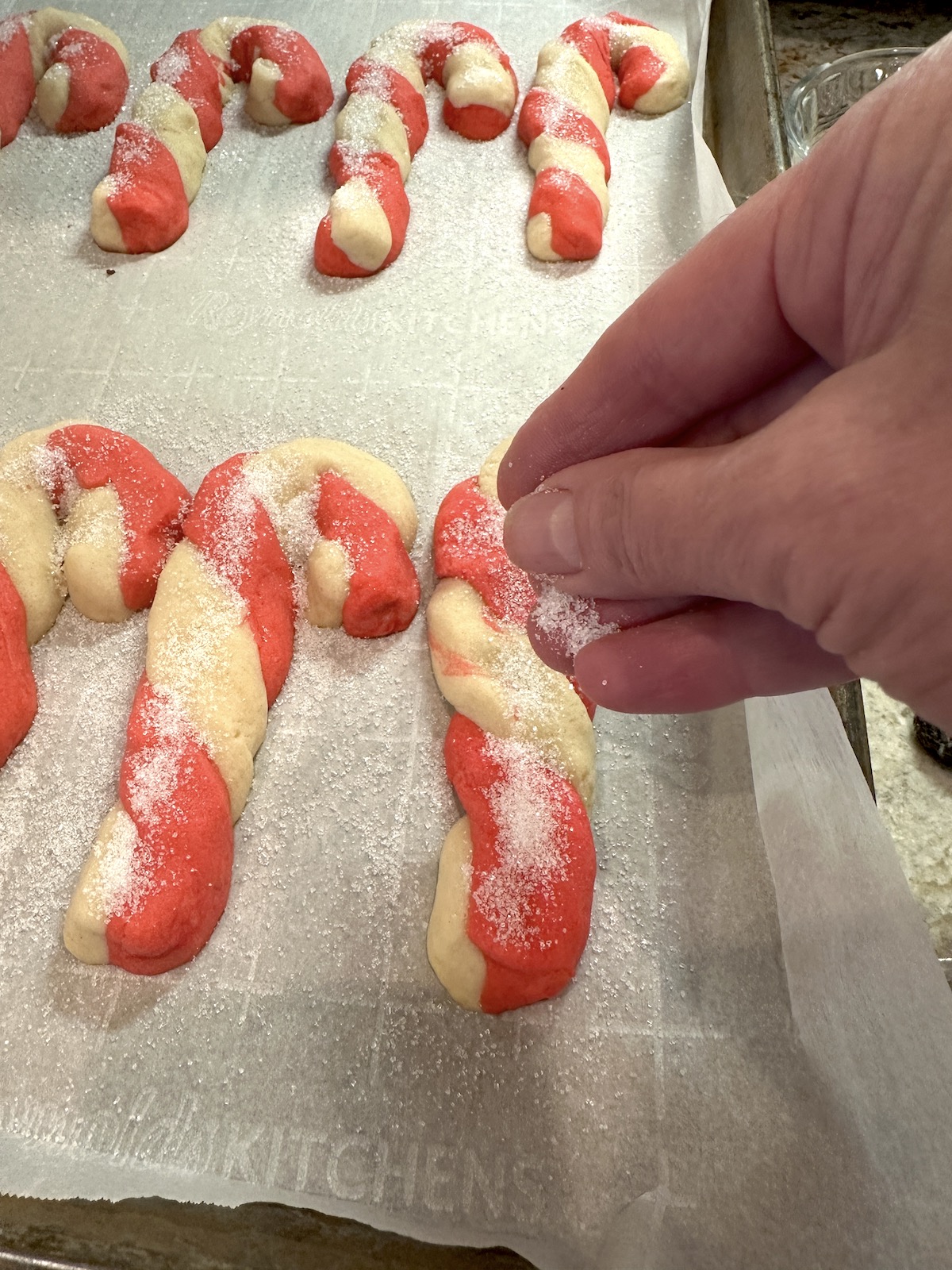 Sugar sprinkled on Christmas candy cane cookies on a baking sheet.