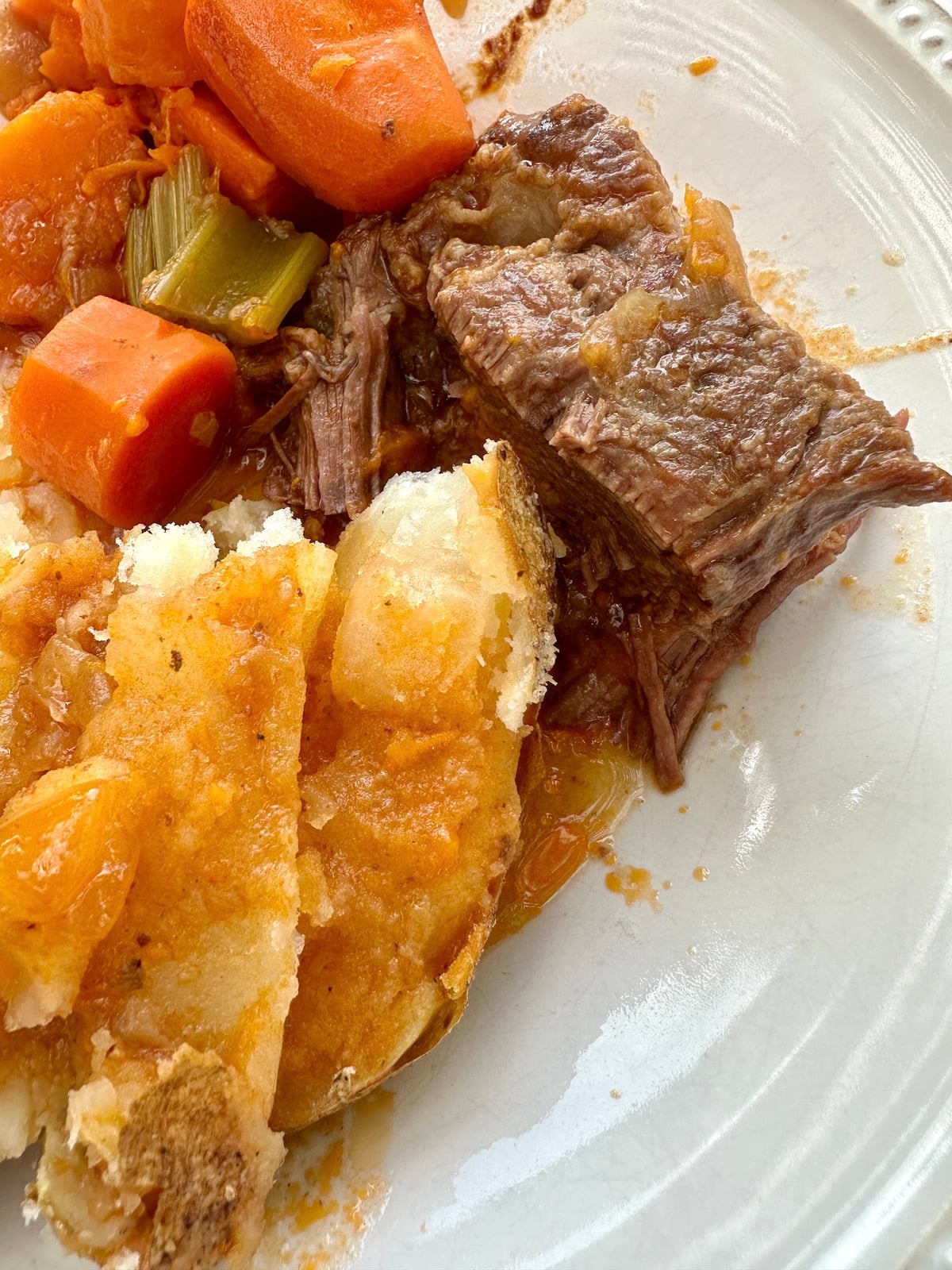 Dutch oven pot roast on a plate with vegetables and potato.