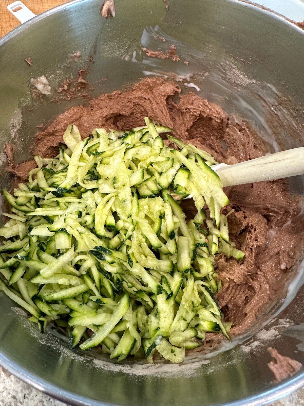 Grated zucchini added to chocolate cake batter in a bowl.