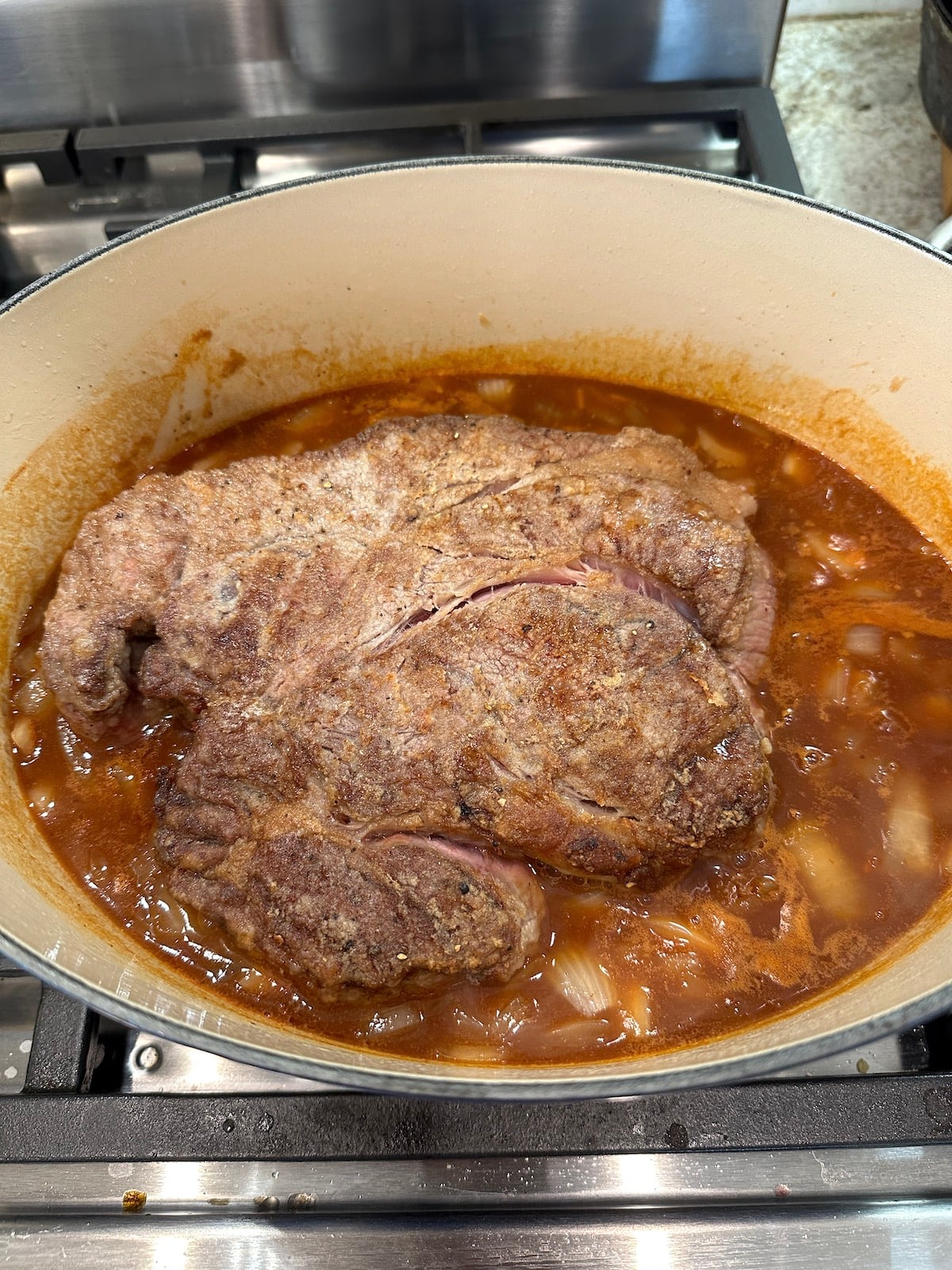 Pot roast in a Dutch oven with broth and vegetables.