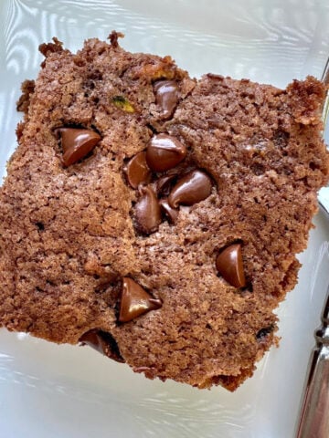 A serving of moist chocolate zucchini cake on a plate with a fork.