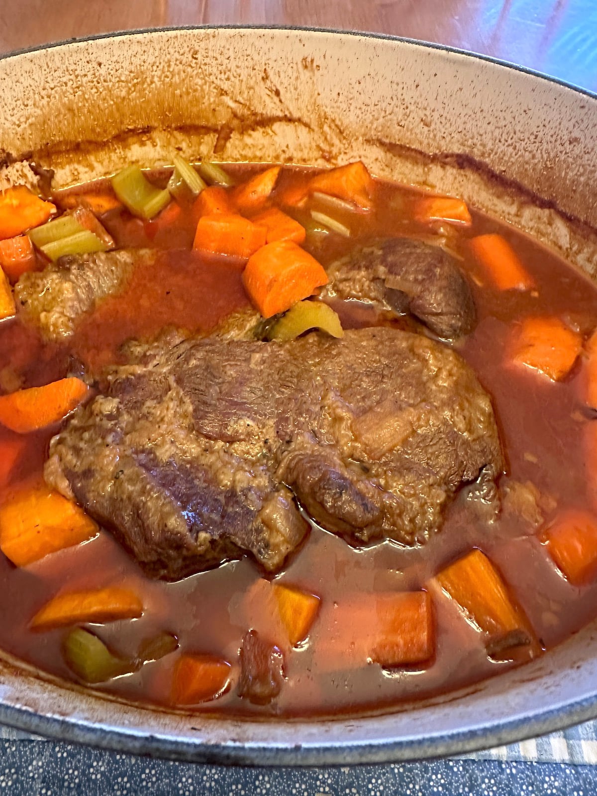 Baked pot roast in a Dutch oven with broth and vegetables.