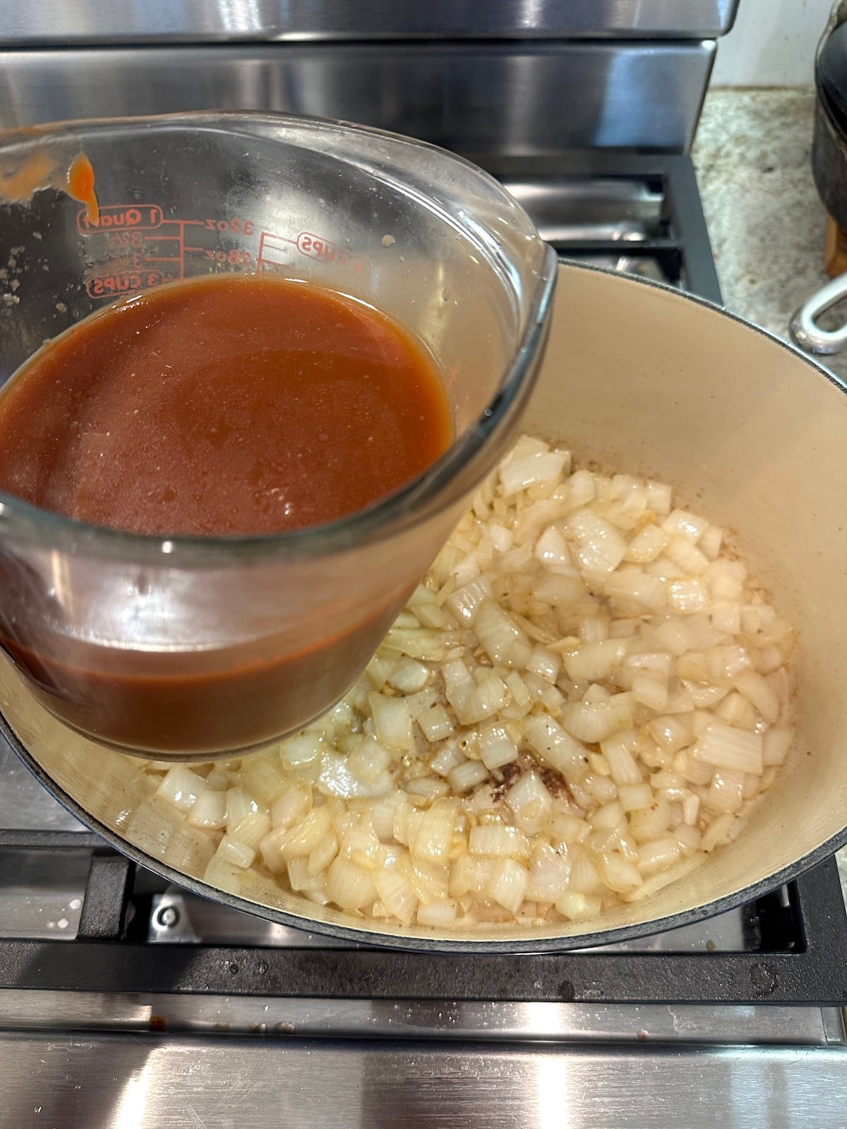 A measuring cup of liquid and a pan of cooked onions.