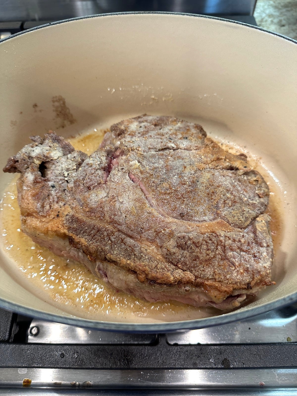 Partially cooked pot roast in a Dutch oven on the stove.
