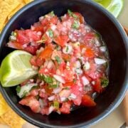 Pico de gallo in a bowl with lime and tortilla chips.