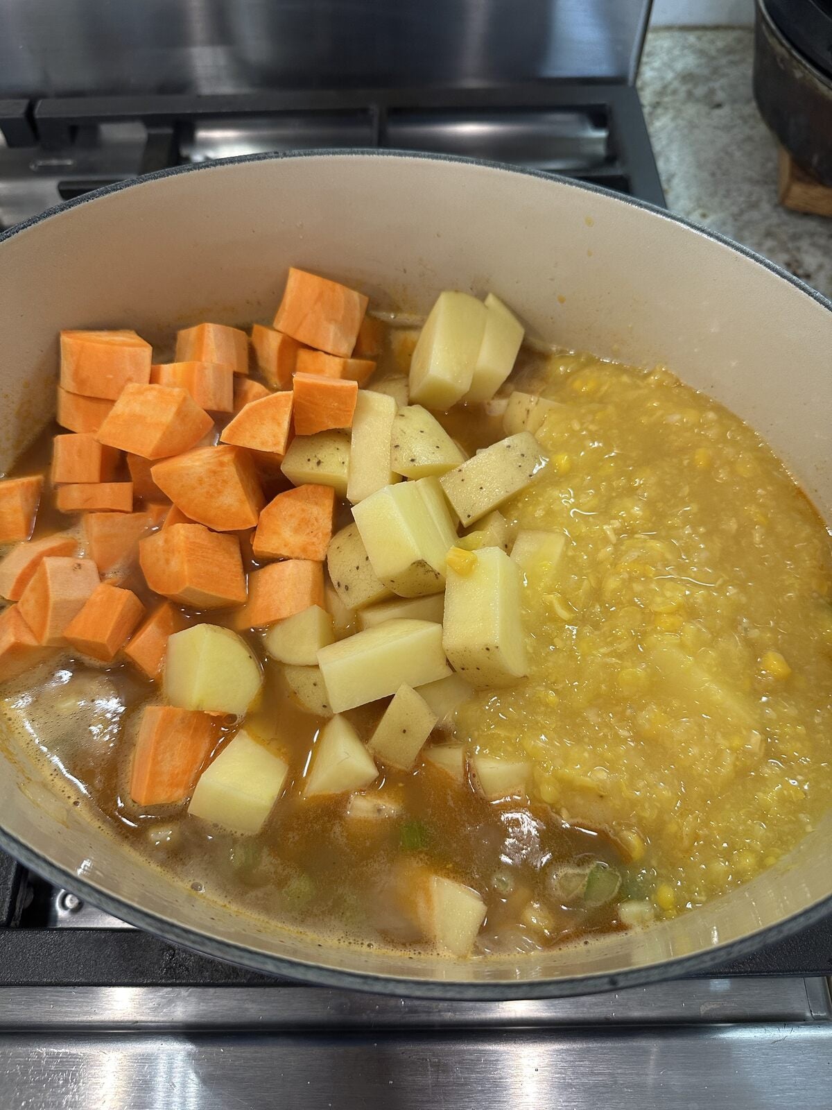 Potatoes and creamed corn with corn soup ingredients in a dutch oven on the stove.
