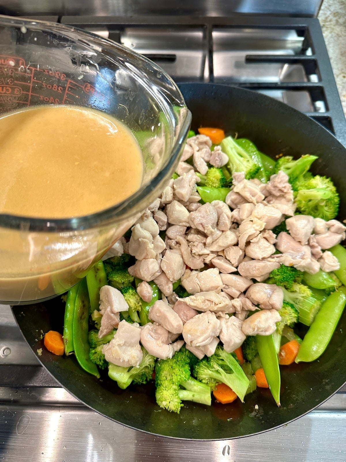 A cup of sauce for cashew chicken stir fry over a pan of veggies and chicken.