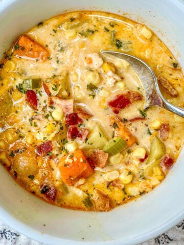 Corn soup with sweet potatoes and bacon in a bowl with a spoon.