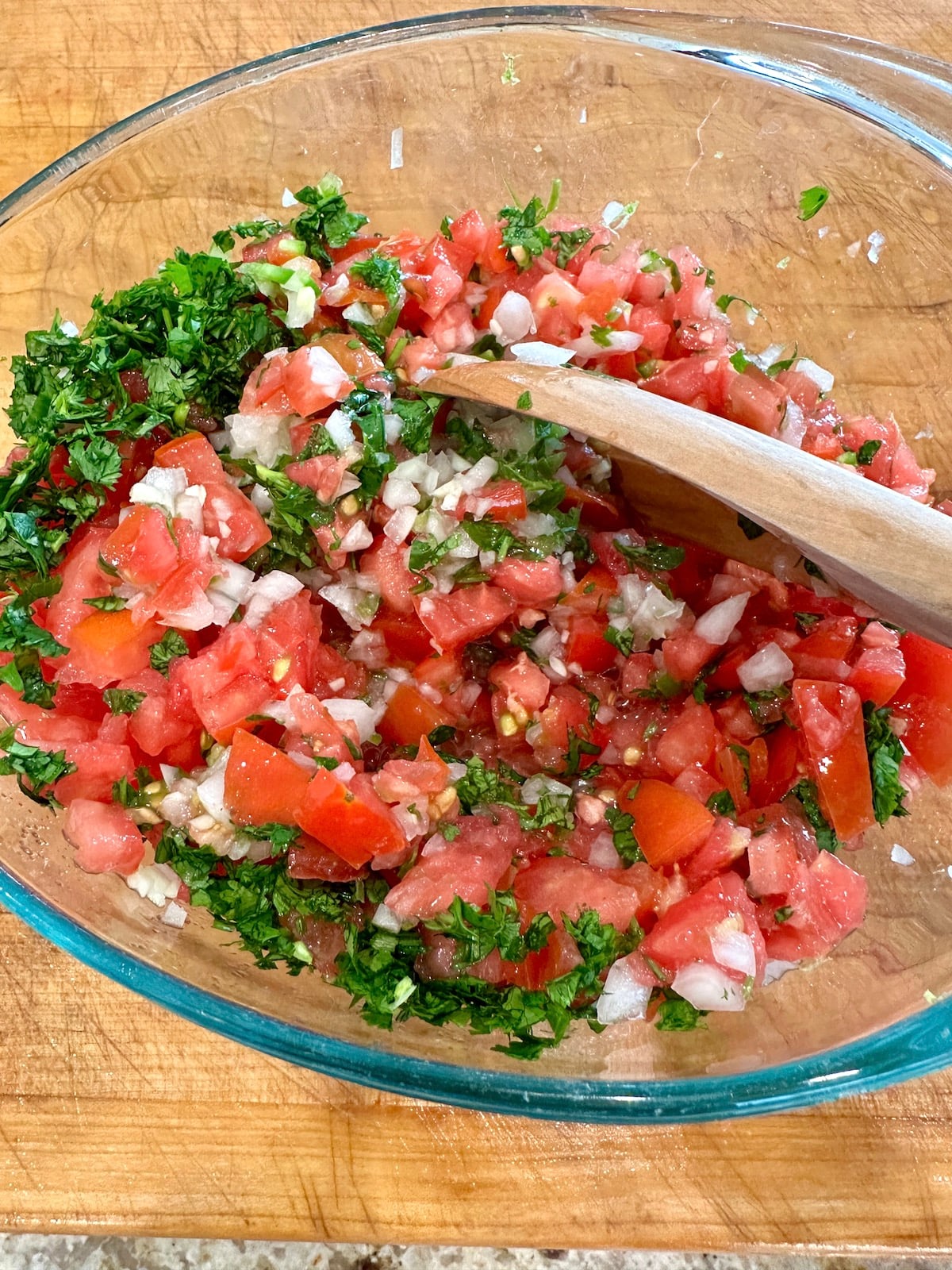 Pico de gallo ingredients in a bowl with a wooden spoon.
