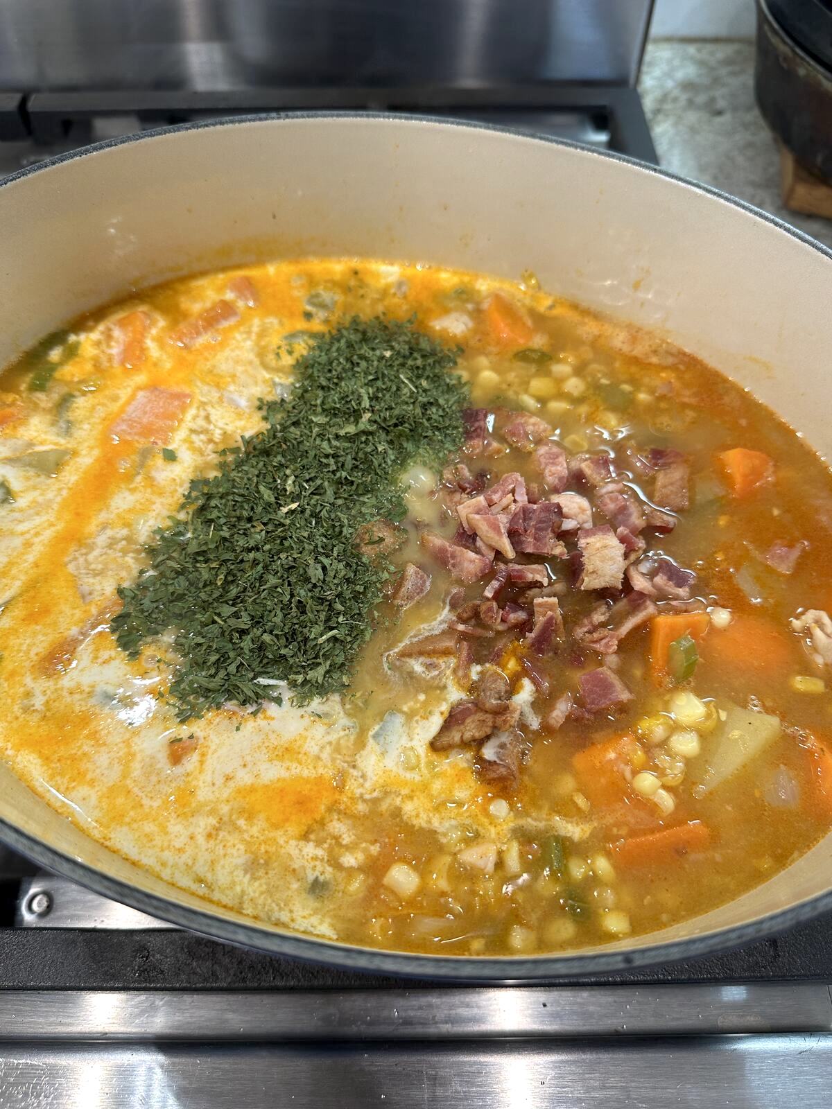 Corn soup ingredients in a saucepan with bacon and parsley.